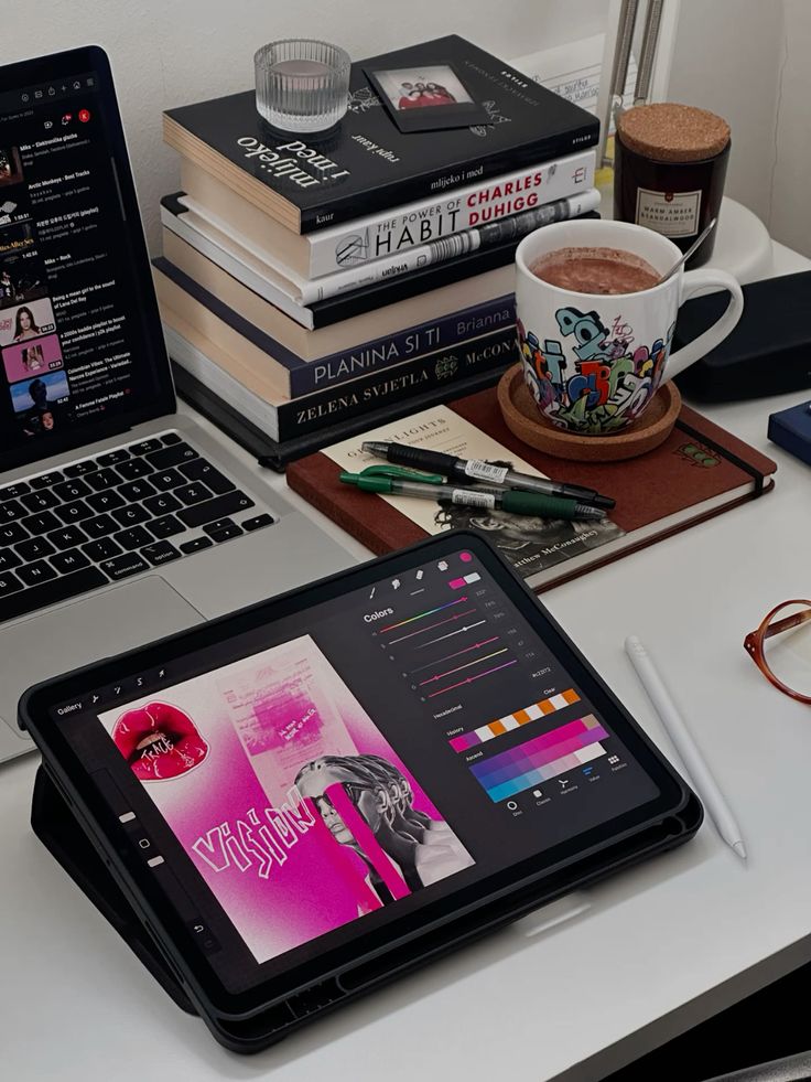 Tablet with design app open on desk, surrounded by books, coffee, and laptop.