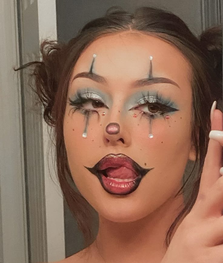 Young woman with artistic clown makeup, highlighting dramatic eyes and glossy lips, poses playfully in front of a mirror.