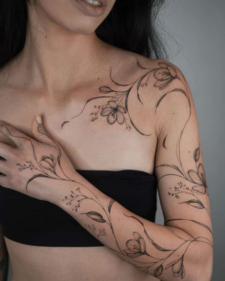Woman with floral arm and shoulder tattoos wearing a black top, showcasing intricate flower design.