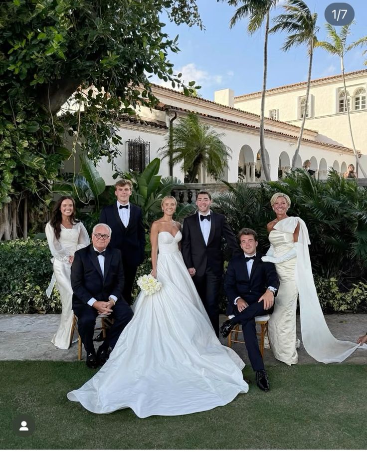 Family posing in elegant attire at an outdoor wedding, lush greenery and a villa backdrop.