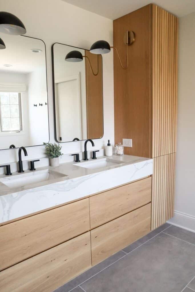 Modern bathroom with double sinks, marble countertop, wood cabinets, and stylish black fixtures.