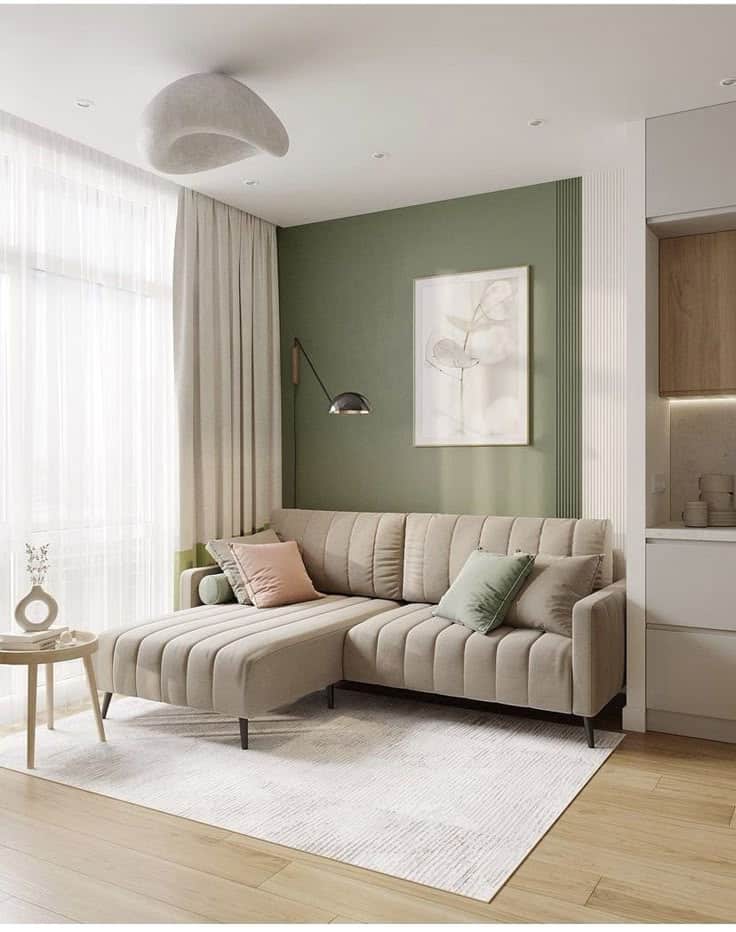 Modern living room with beige sectional sofa, green accent wall, and natural light. Cozy and stylish interior design.