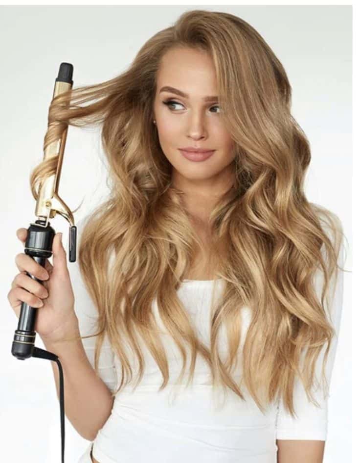 Woman using curling iron to style long, wavy blonde hair.