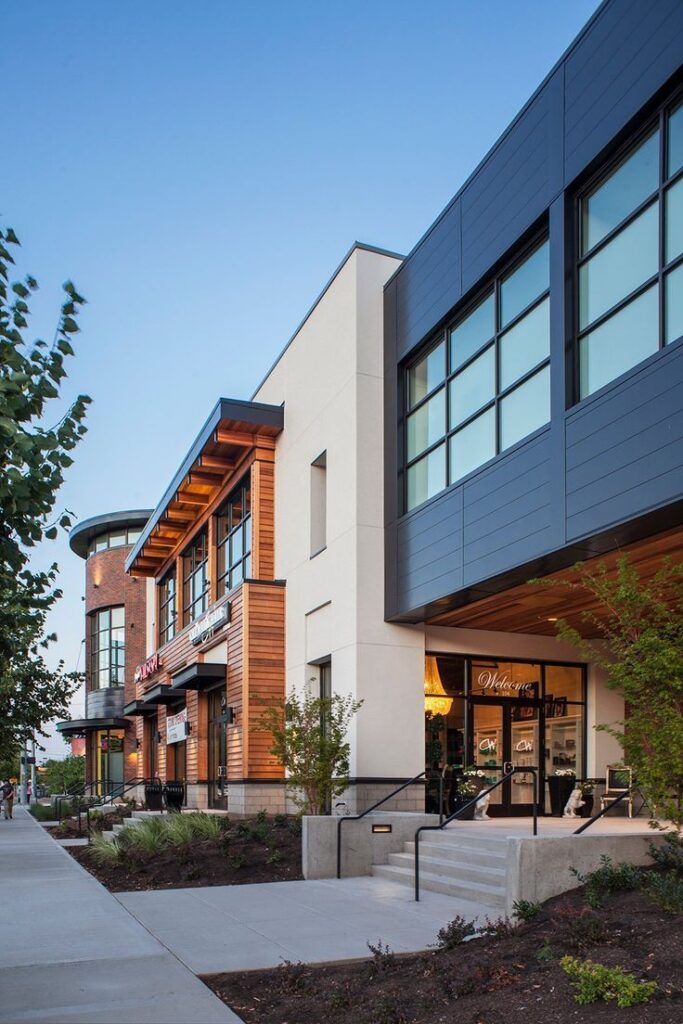Modern shopping center exterior with large windows and retail signage, set against a clear blue sky.