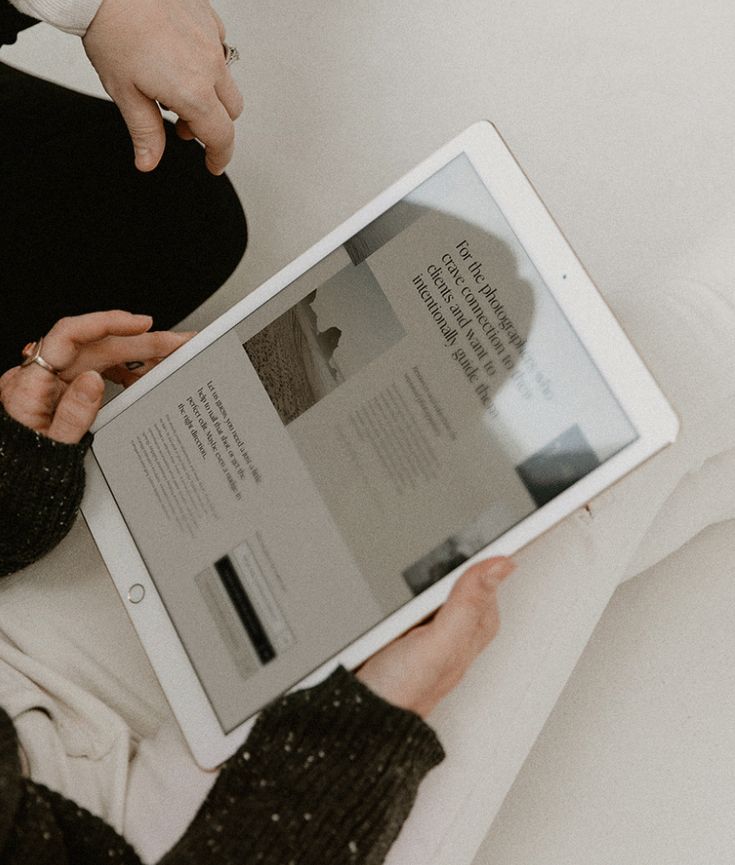 Person reading content on a tablet, featuring photography-related text and images, with cozy, neutral-toned surroundings.