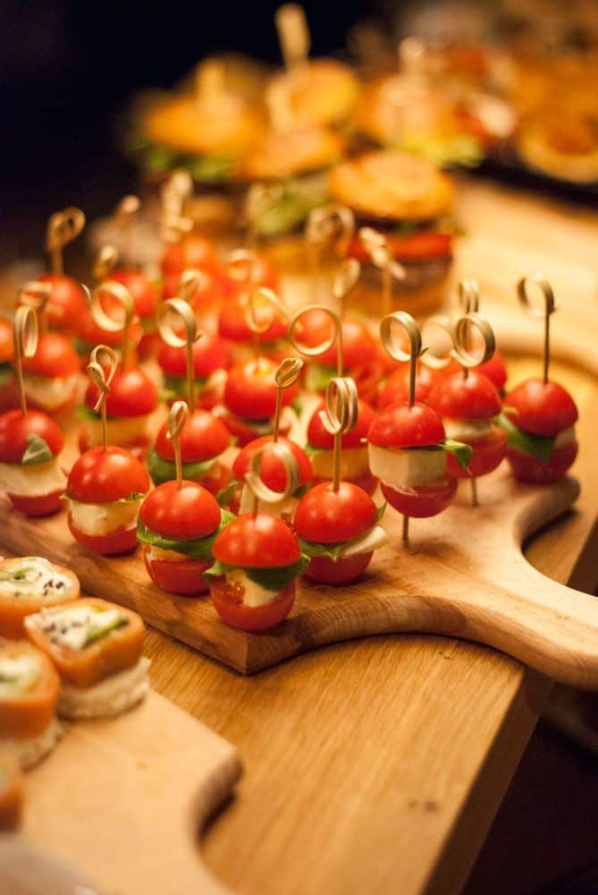 Cherry tomato, mozzarella, and basil appetizers on skewers displayed on a wooden board. Perfect for party snacks.
