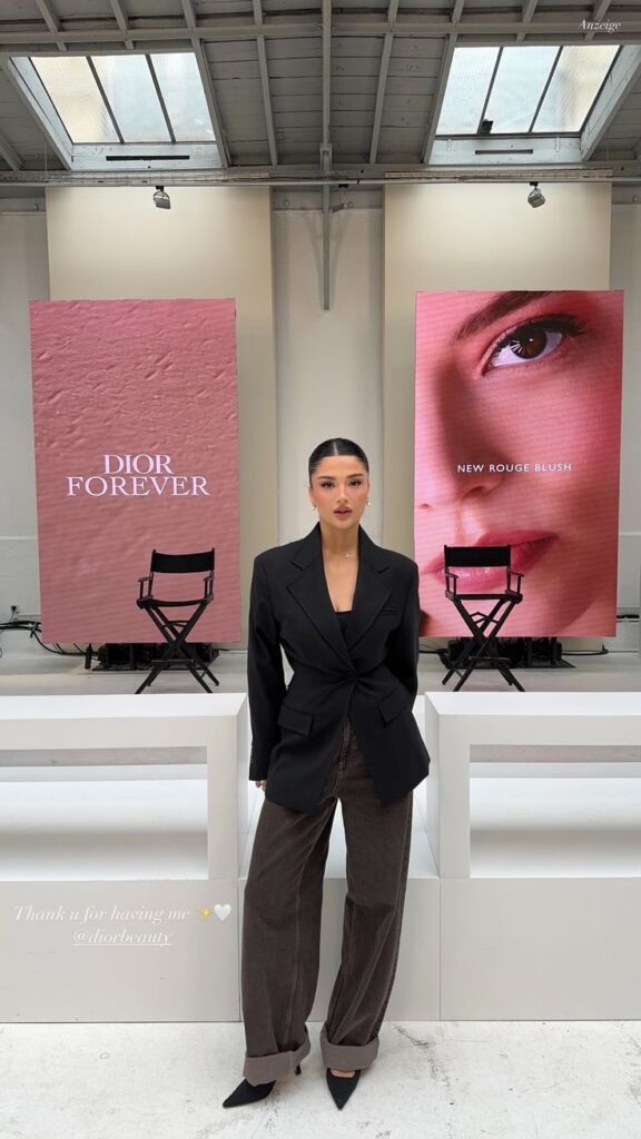 Woman in stylish outfit at Dior event with Dior Forever and New Rouge Blush displays in the background.