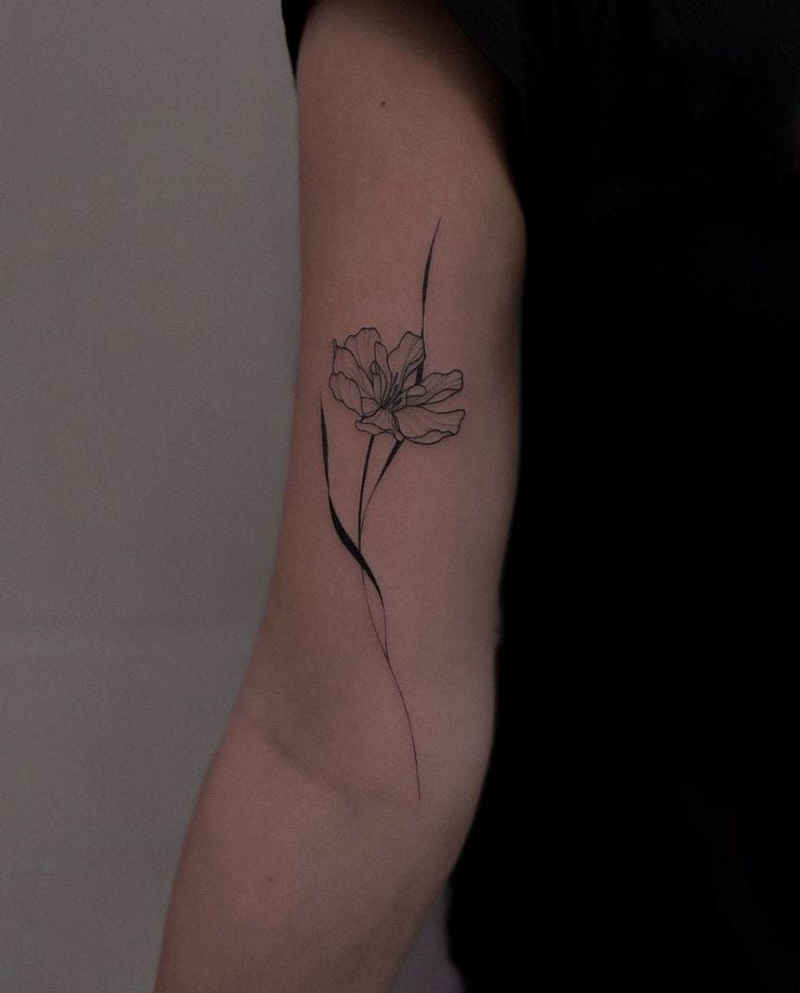 Minimalist flower tattoo on a person's upper arm, showcasing elegant line art.