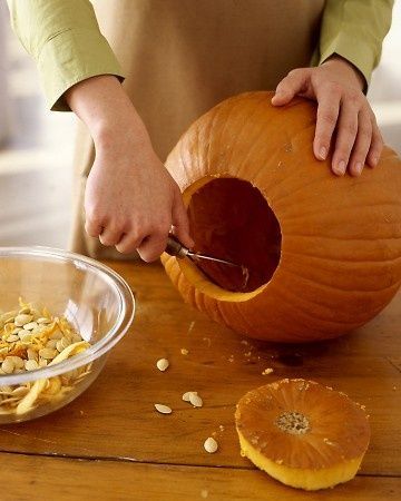 Person carving pumpkin with a scoop, seeds placed in a bowl, top off the pumpkin, on a wooden table. Perfect for Halloween.
