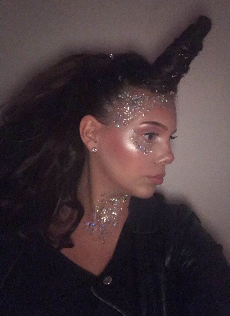 Young woman with unicorn horn and glitter makeup, smiling in leather jacket. Fantasy costume portrait.