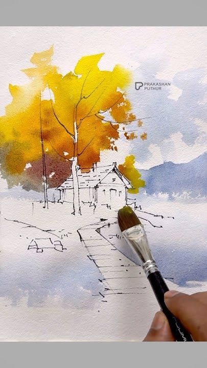 Hand painting a watercolor landscape with trees and a house, featuring vibrant autumn colors and a soft blue sky.