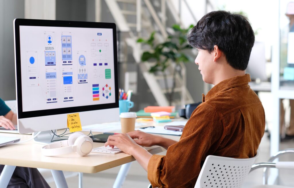 Person designing app interface on a computer in modern office, focusing on user experience and layout design.