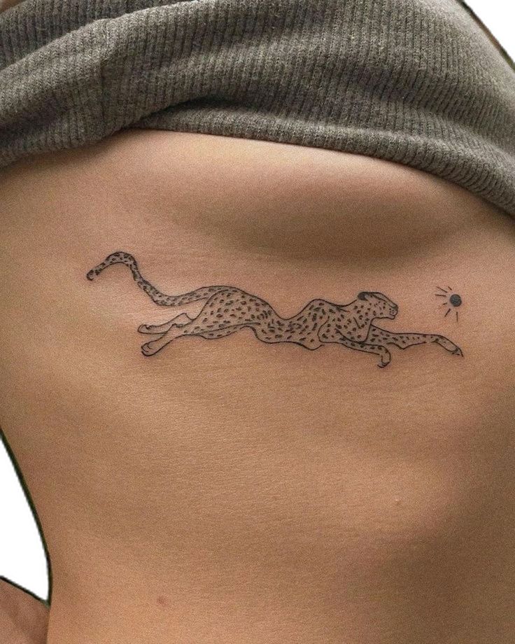 Leaping cheetah tattoo on rib, black ink with minimal details, sun in background, under gray fabric.