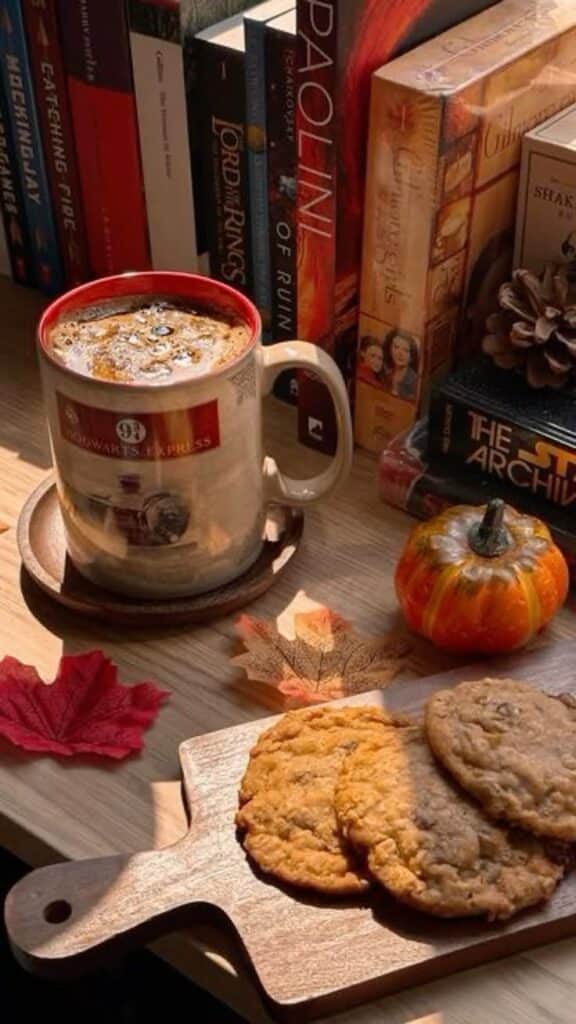 Cozy autumn scene with a mug of coffee, cookies, small pumpkin, and books on a wooden table.