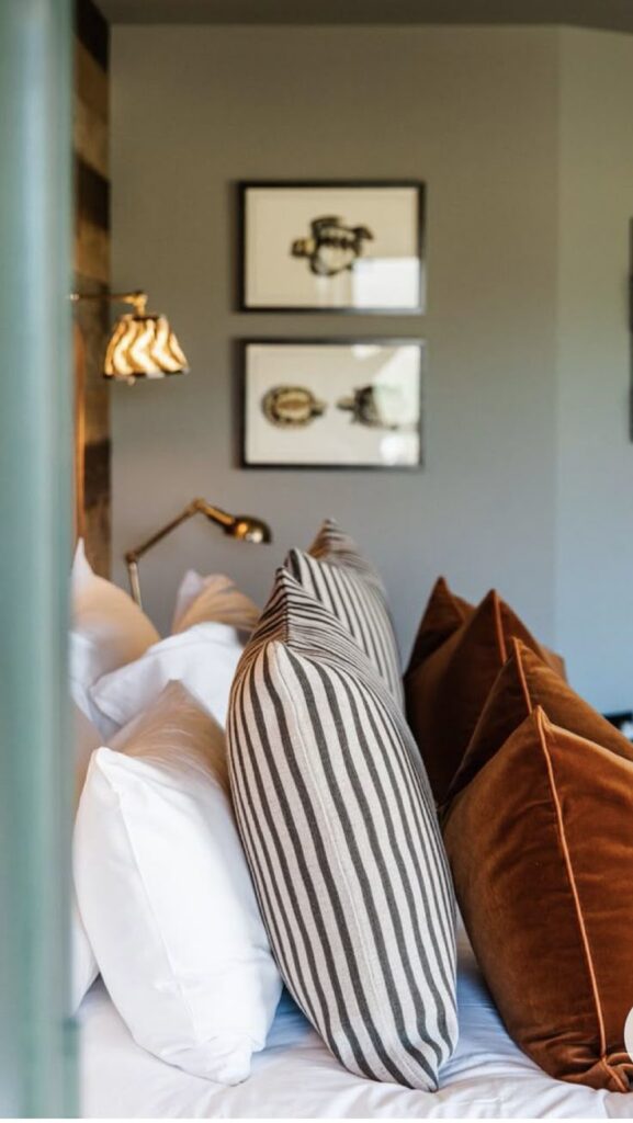 Stylish bedroom with striped and velvet pillows, modern wall art, and cozy lighting for a warm ambiance.