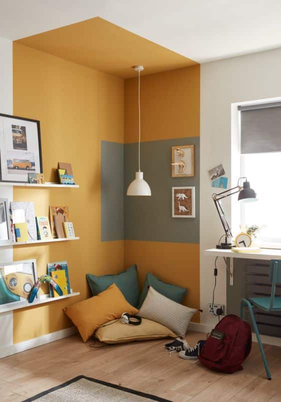 Cozy reading nook with yellow and green cushions, a hanging lamp, bookshelf, and study desk for a modern, inviting space.