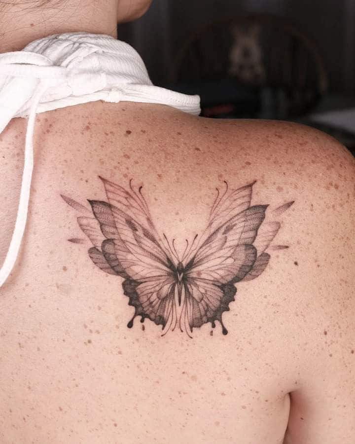 Butterfly tattoo on upper back with detailed black and gray shading on skin.