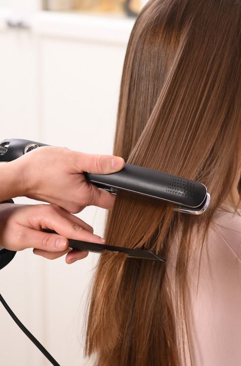 Hair being straightened with a flat iron and comb, achieving smooth, sleek results in a salon setting.