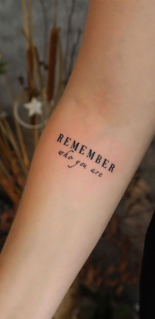 Tattoo on forearm reading Remember who you are in black lettering with background decor.