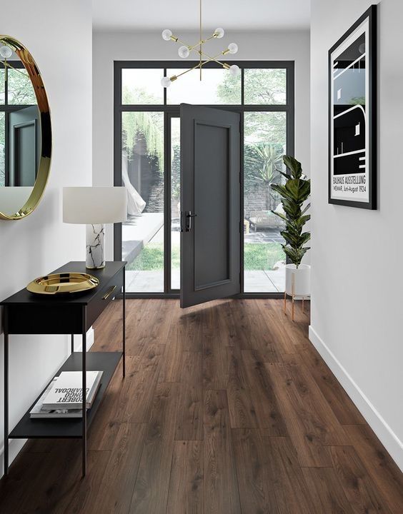 Modern entryway with wood flooring, black console table, and open glass door leading to a garden. Elegant decor style.