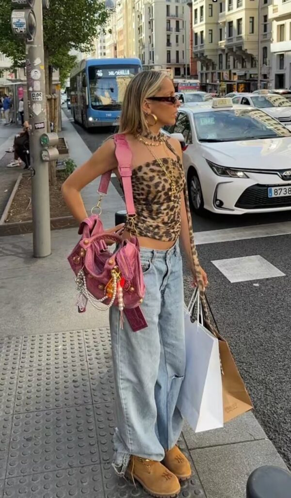 Fashionable woman in leopard top, jeans, holding shopping bags and pink bag on city street.