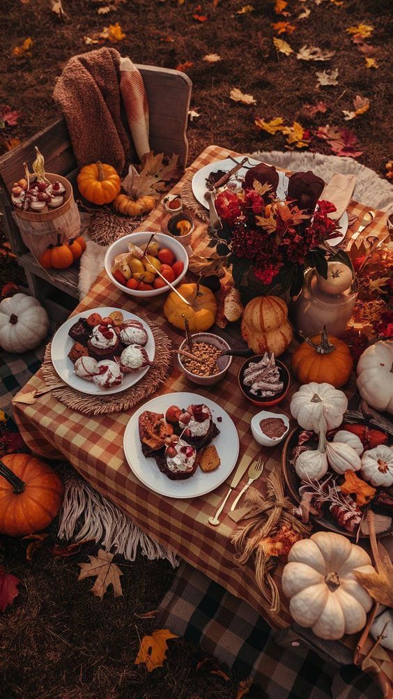Autumn picnic setup with pumpkins, desserts, and fall leaves on a plaid blanket, capturing cozy seasonal vibes.