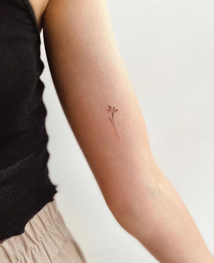 Minimalist flower tattoo on the inner arm, showcasing delicate artistic design on a blurred background.