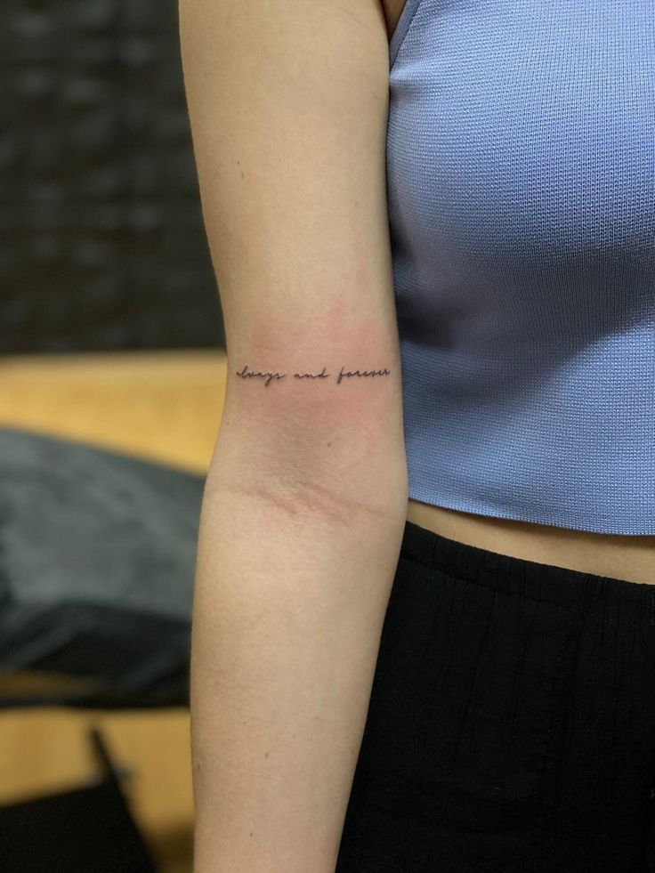 Arm tattoo with cursive script saying always and forever, wearing a blue top.