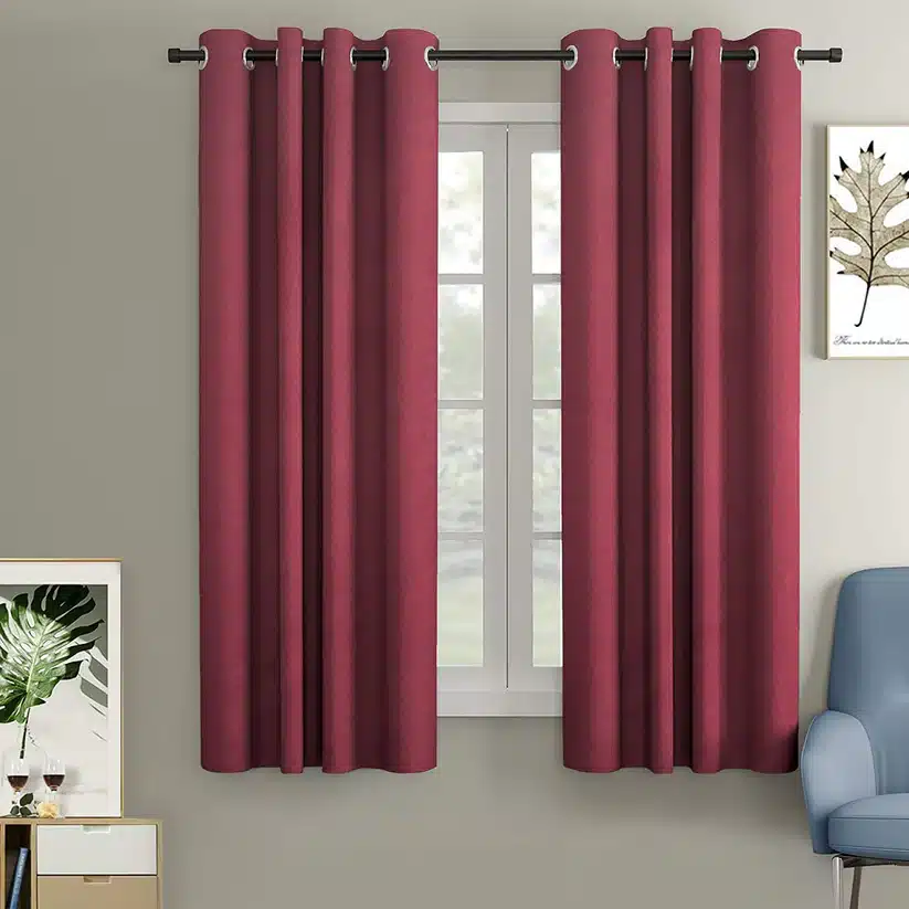 Room with red curtains on a window, modern decor, and art on walls. Cozy ambiance with a blue chair.
