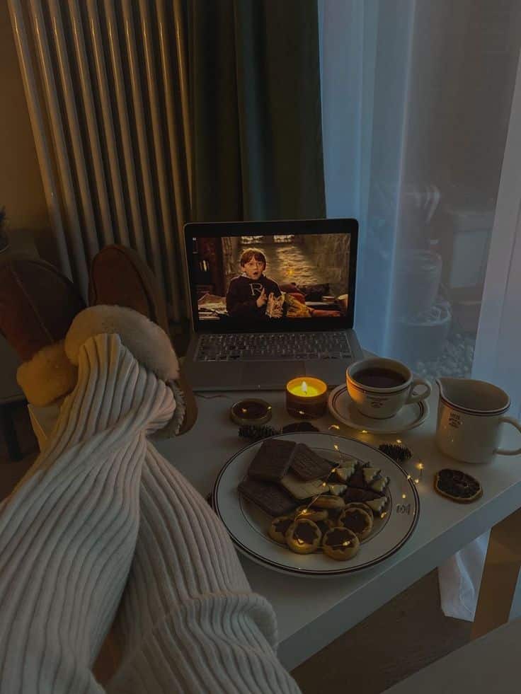 Cozy night in with laptop, snacks, hot drinks, and a candlelit atmosphere. Perfect for relaxing at home.