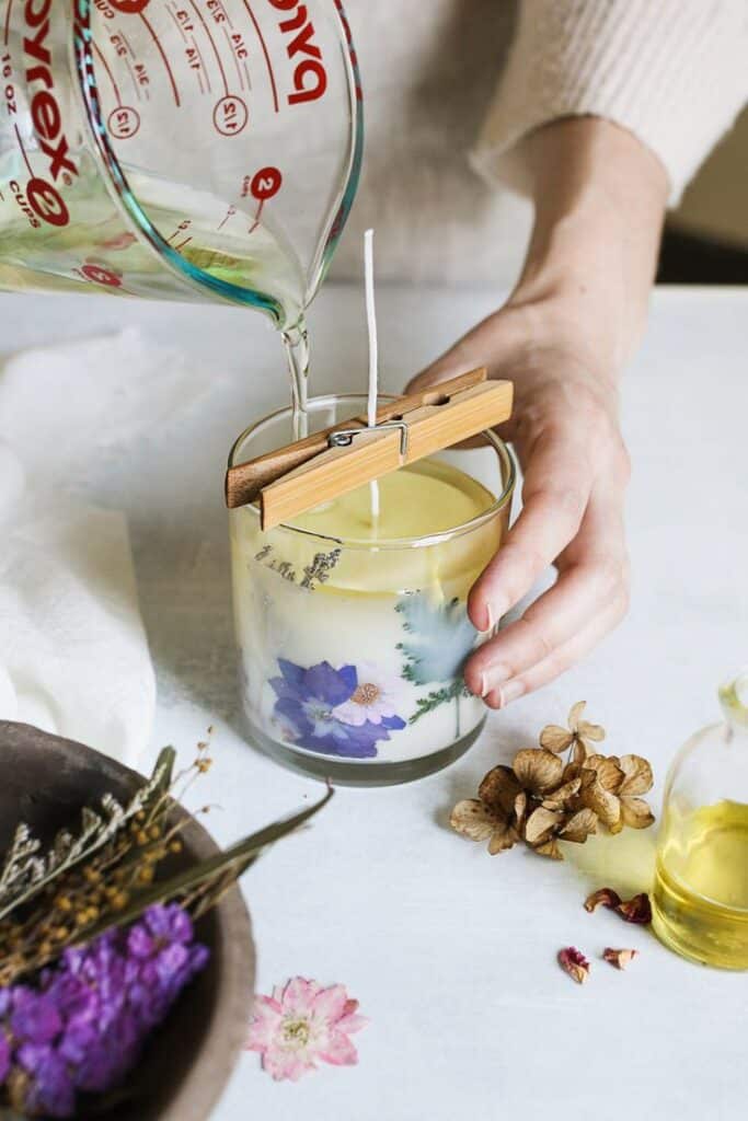 Pouring wax into a floral-decorated candle jar for DIY candle making at home.