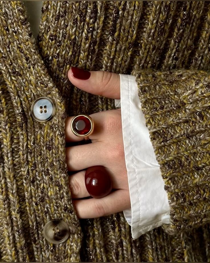 Close-up of hand wearing red gemstone rings on knit sweater, showcasing fashion and style.