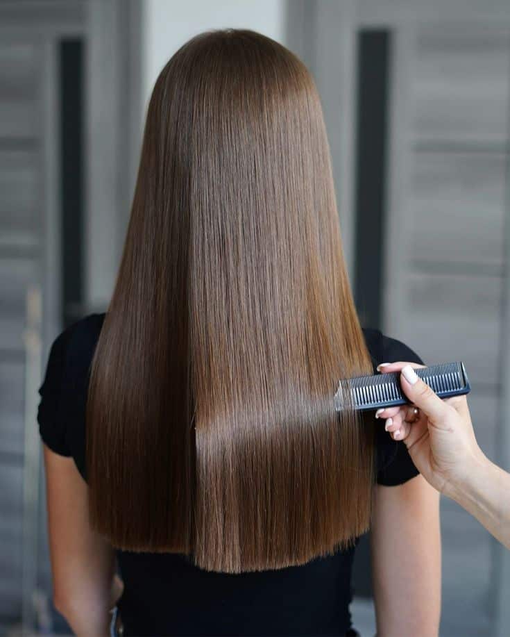 Straight, shiny brown hair being combed, showcasing smooth and healthy hair maintenance.
