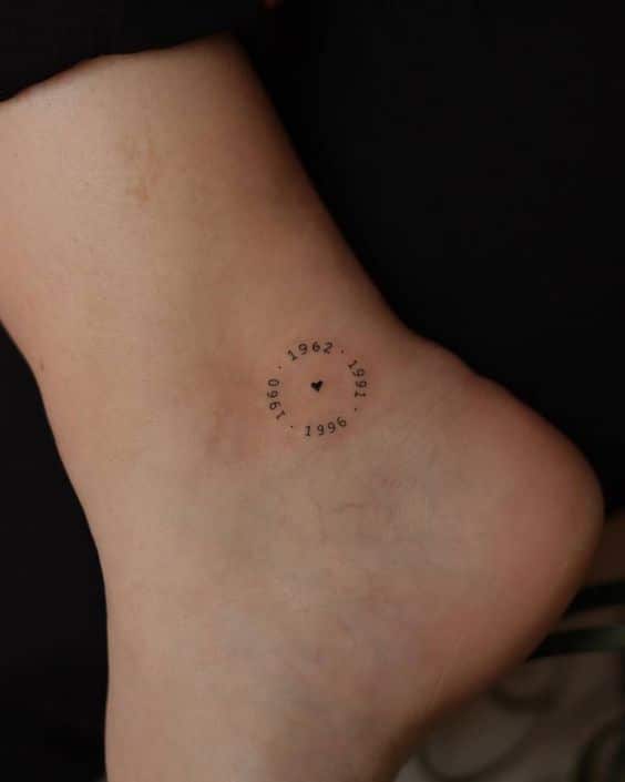 Minimalist ankle tattoo with years encircling a heart design.
