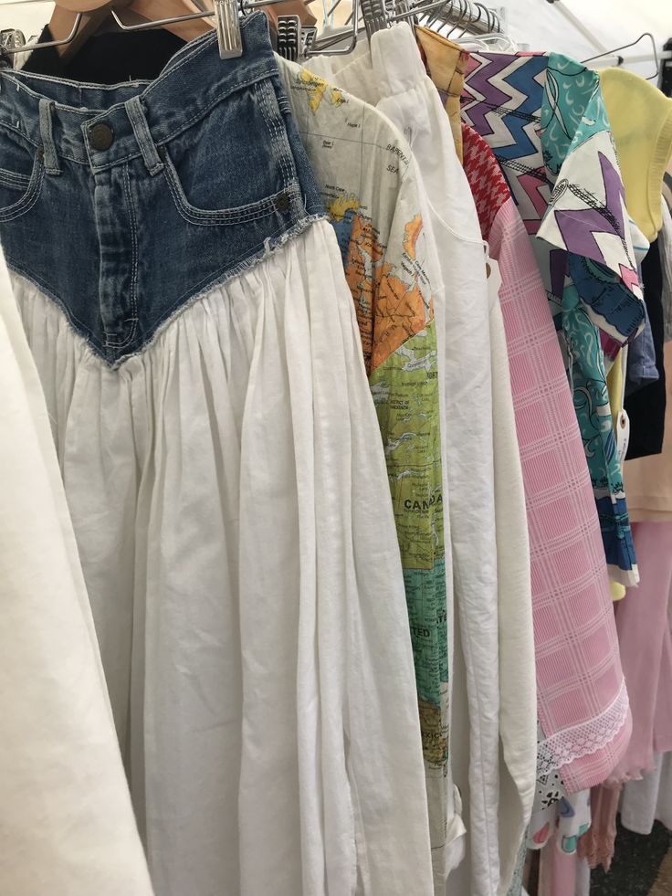 A rack of eclectic vintage clothing, featuring a denim and white skirt, colorful patterns, and a map-themed shirt.