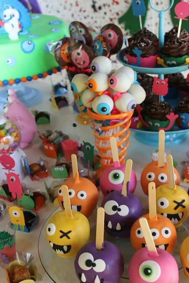 Colorful monster-themed dessert table with candy apples, cupcakes, and cake pops. Perfect for a fun party!