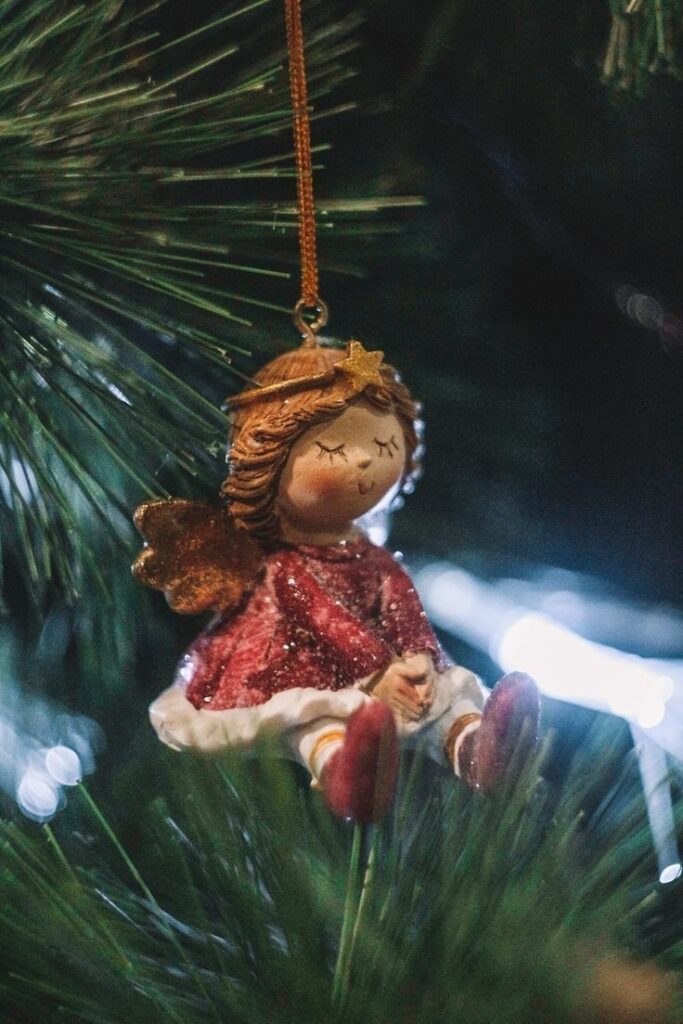 _ 8 Angel ornament in red dress hanging on Christmas tree branch, festive and serene holiday decoration. | Sky Rye Design Angel ornament in red dress hanging on Christmas tree branch, festive and serene holiday decoration.
