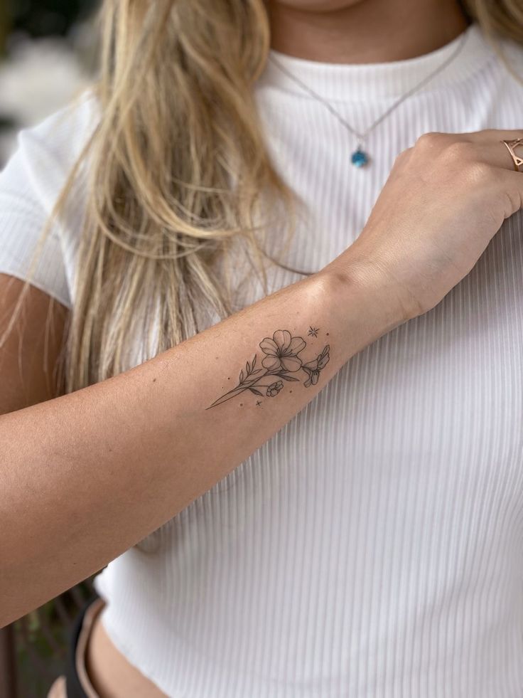 Delicate floral tattoo on a woman's forearm with a white ribbed shirt in the background.