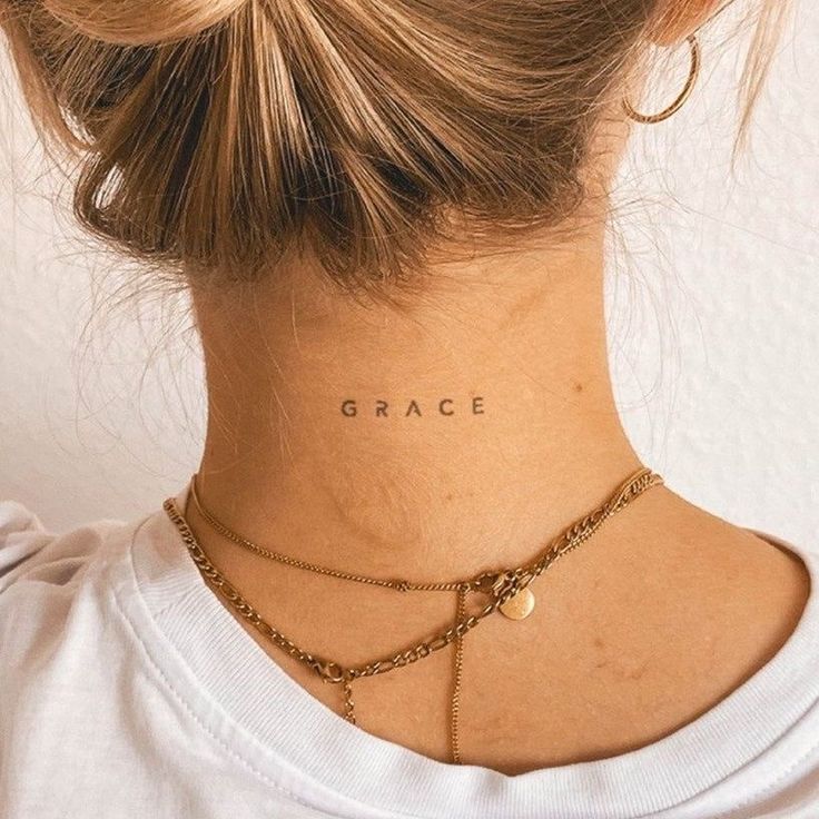 Neck tattoo reading Grace above gold necklaces and hoop earring on blonde-haired person with hair in a bun.