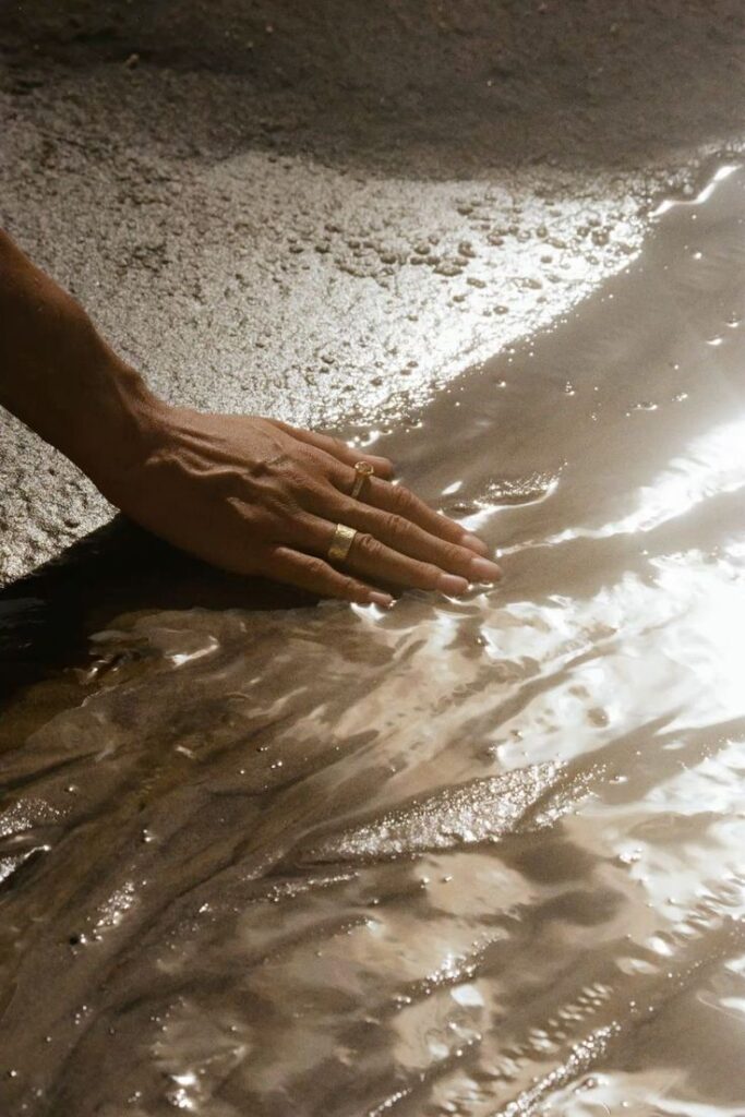 Hand touching wet sand with gentle sunlight reflections.