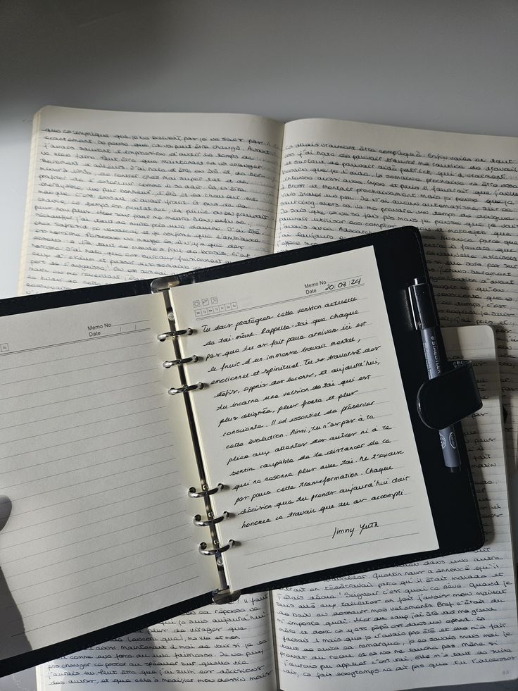 Open notebooks with handwritten French text and a pen, lying on a table, showcasing creative writing.