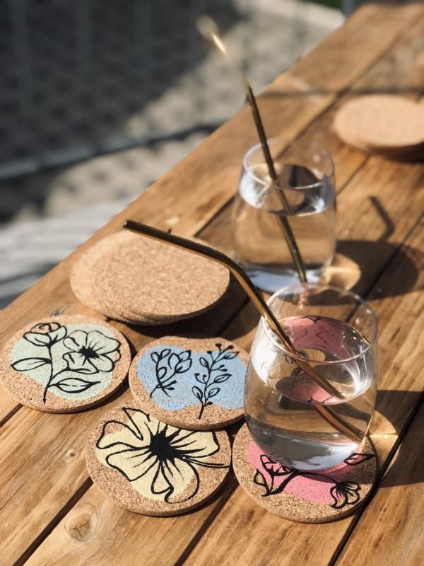 Colorful floral cork coasters on a wooden table with glasses and metal straws, perfect for eco-friendly home decor.