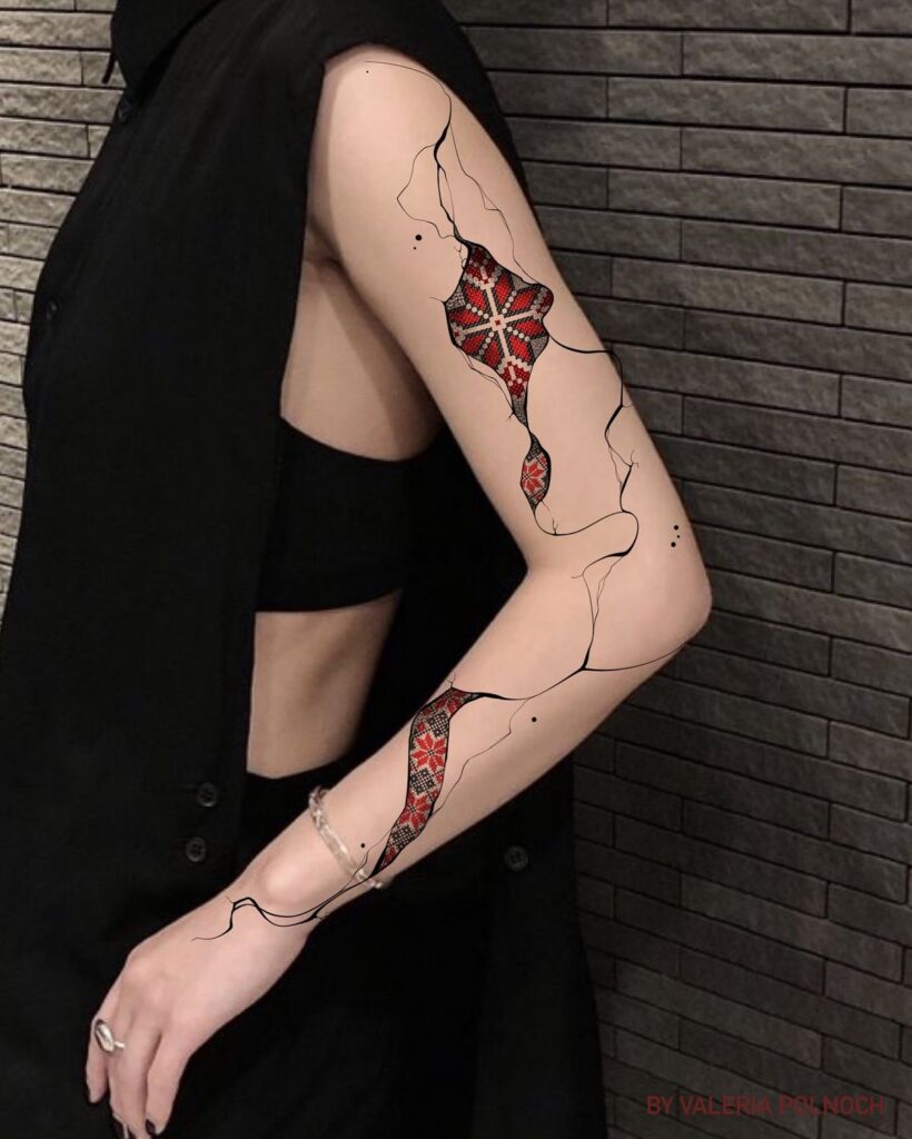 Creative geometric tattoo with red, white, and black patterns on a person's arm, wearing a sleeveless black outfit.