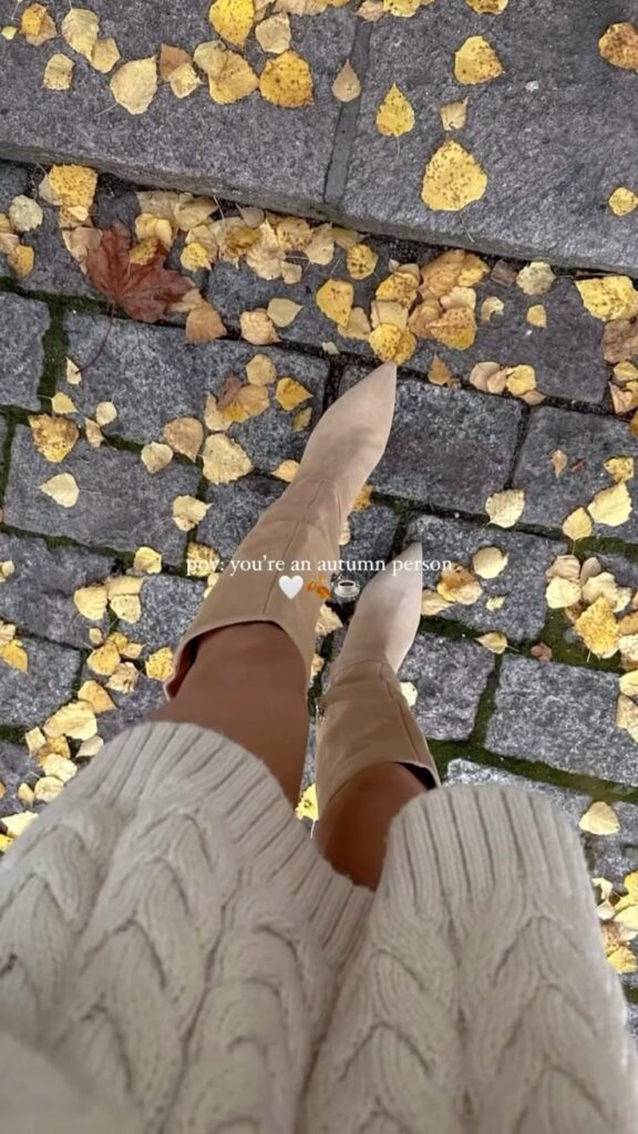 Knit sweater and boots on cobblestone path with fallen autumn leaves. Cozy fall fashion vibes.