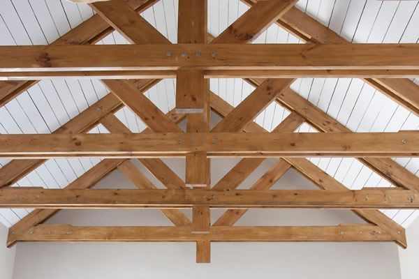 Exposed wooden trusses against white ceiling, highlighting architectural design and natural wood finish.