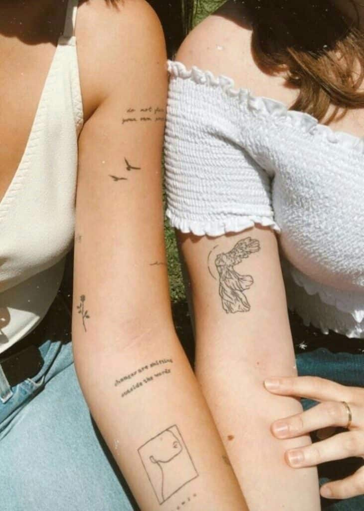 Two people sitting side by side, showcasing small tattoos on their arms, wearing casual tops and jeans.