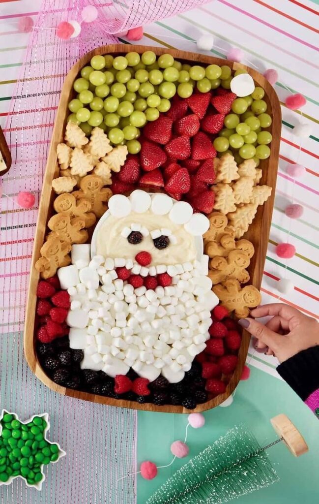 Festive fruit and cookie platter with holiday-themed design, garnished with marshmallows and berries.