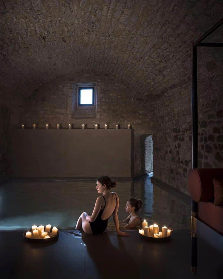 Two women relax in a candlelit stone spa pool, creating a serene and calming atmosphere.