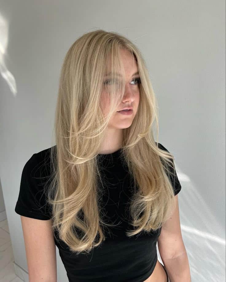 90s layers 👩🏼 Woman with long, layered blonde hair and black crop top in natural light, looking to the side against a neutral background. | Sky Rye Design Woman with long, layered blonde hair and black crop top in natural light, looking to the side against a neutral background.