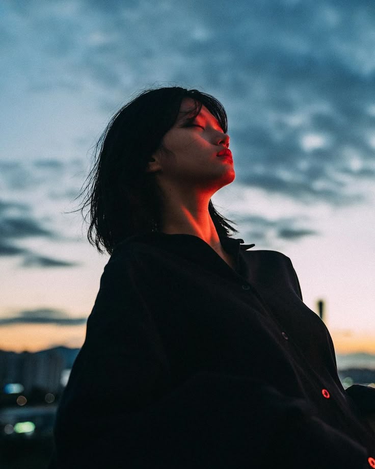 Person in dark clothing enjoys a peaceful sunset moment with a cloudy sky backdrop.